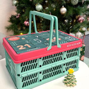 Back Adventskalender 2025 von Meine Backbox im praktischen Einkaufskorb vor einem geschmückten Tannenbaum