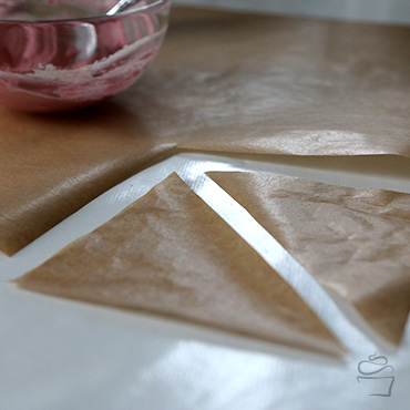Ein Quadrat aus Backpapier ausschneiden und teilen, so dass zwei Dreiecke entstehen. Die Größe kann variieren, sollte aber noch handlich sein.